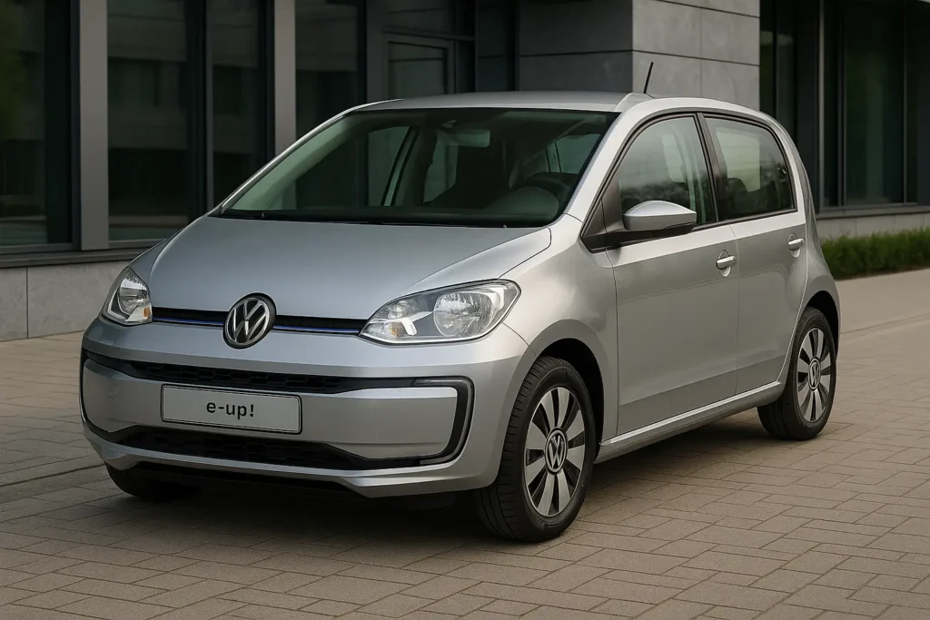 Volkswagen e-up! 2025 in Silber-Metallic, geparkt auf einem gepflasterten Vorplatz mit moderner Glasfassade